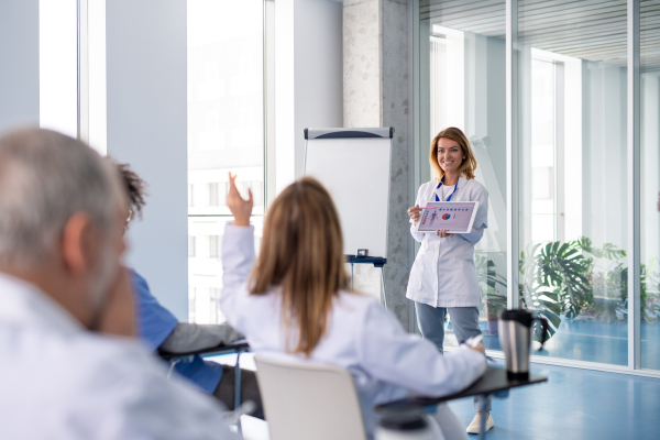 Female doctor as speaker at conference for group of healtcare workers, medical team sitting and listening presenter. Medical experts attending an education event, seminar in board room.