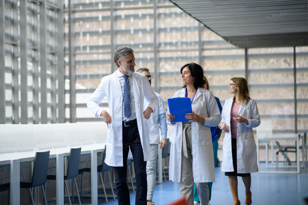 Team of doctors discussing test results, walking across corridor. Colleagues discussing patients diagnosis in modern hospital, clinic.