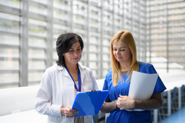 Two female doctors discussing test results, walking across corridor. Colleagues discussing patients diagnosis. Women in medicine science