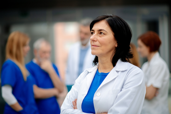 Portrait of beautiful female doctor standing in front of team of doctors. Colleagues, doctors team discussing patients diagnosis. in modern hospital, clinic.