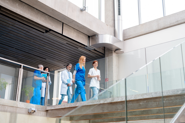 Team of doctors walking across hospital corridor. Colleagues, doctors team discussing medical case. Low angle shot with copy space.