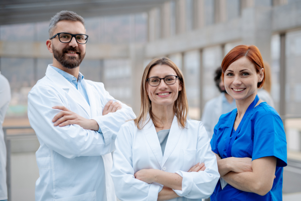 Portrait of three doctors, looking at camera and smiling. Healthcare team in medical uniforms in hospital.