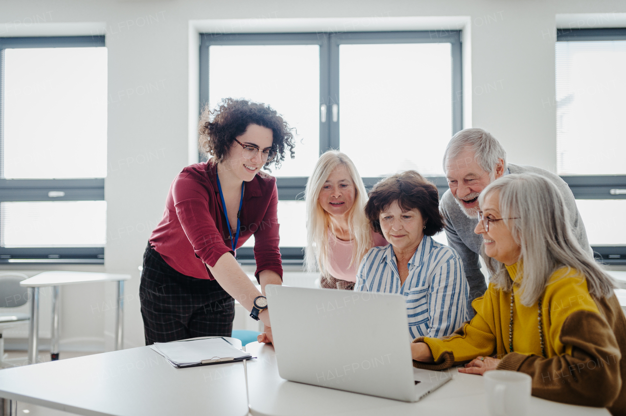 Teacher explaining senior students how to work with laptop, internetbanking. Elderly people attending computer and technology education class.