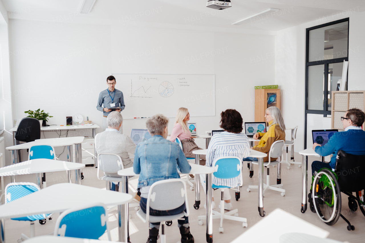 Teacher explaining senior students how to work with laptop, internet. Elderly people attending computer and technology education class.