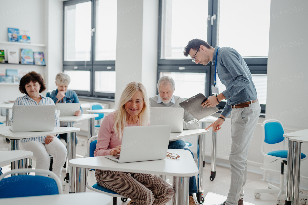 Teacher explaining senior students how to work with laptop, internet. Elderly people attending computer and technology education class.