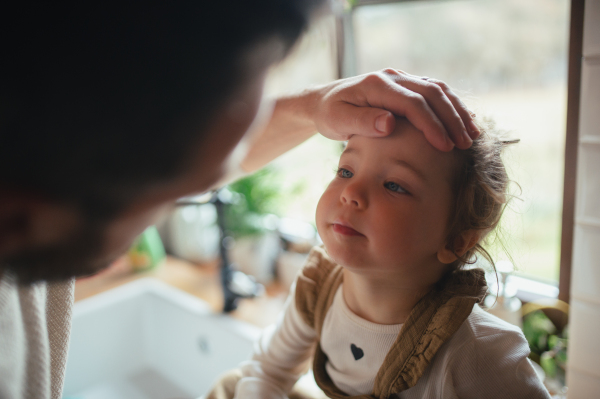 Sick girl with a fever and cold at home. Father touching little daughter forehead, checking her temperature.