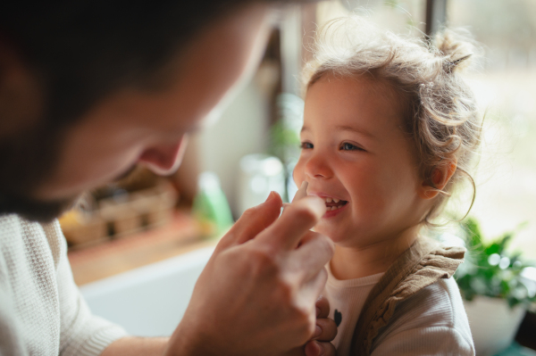 Sick girl with cold at home has stuffy nose. Father helping little daughter, using nasal spray in his nose