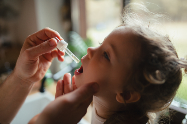 Father giving his daughter medicine with medicine dropper, cough syrup or fever medicine. Sick girl with a fever and cold at home.