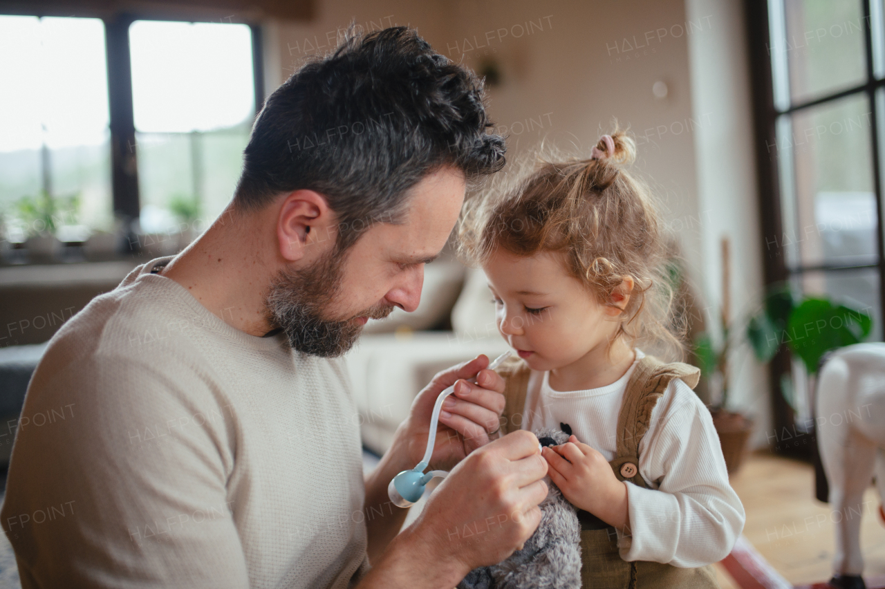 Father helping daughter with stuffy nose, using nasal suction bulb to clear mucus from his nose