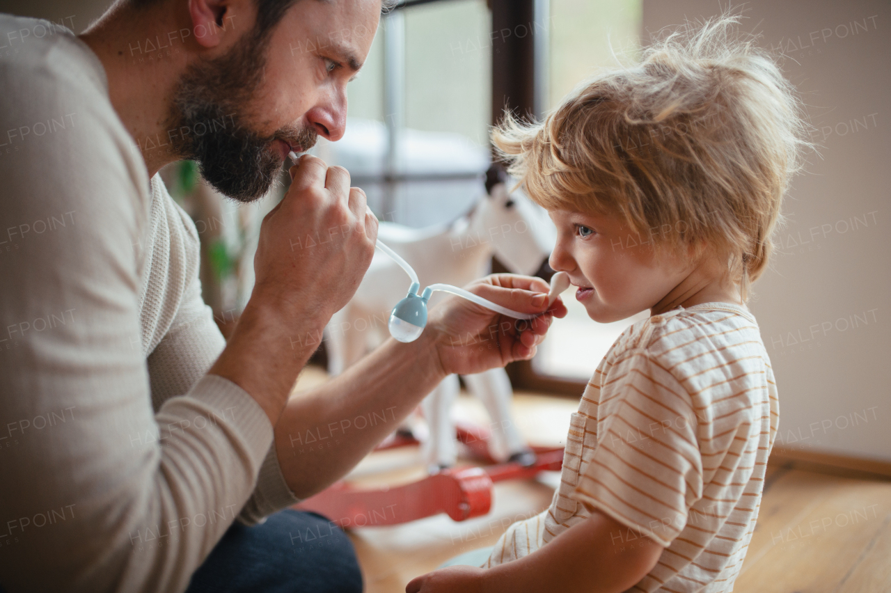 Father helping son with stuffy nose, using nasal suction bulb to clear mucus from his nose