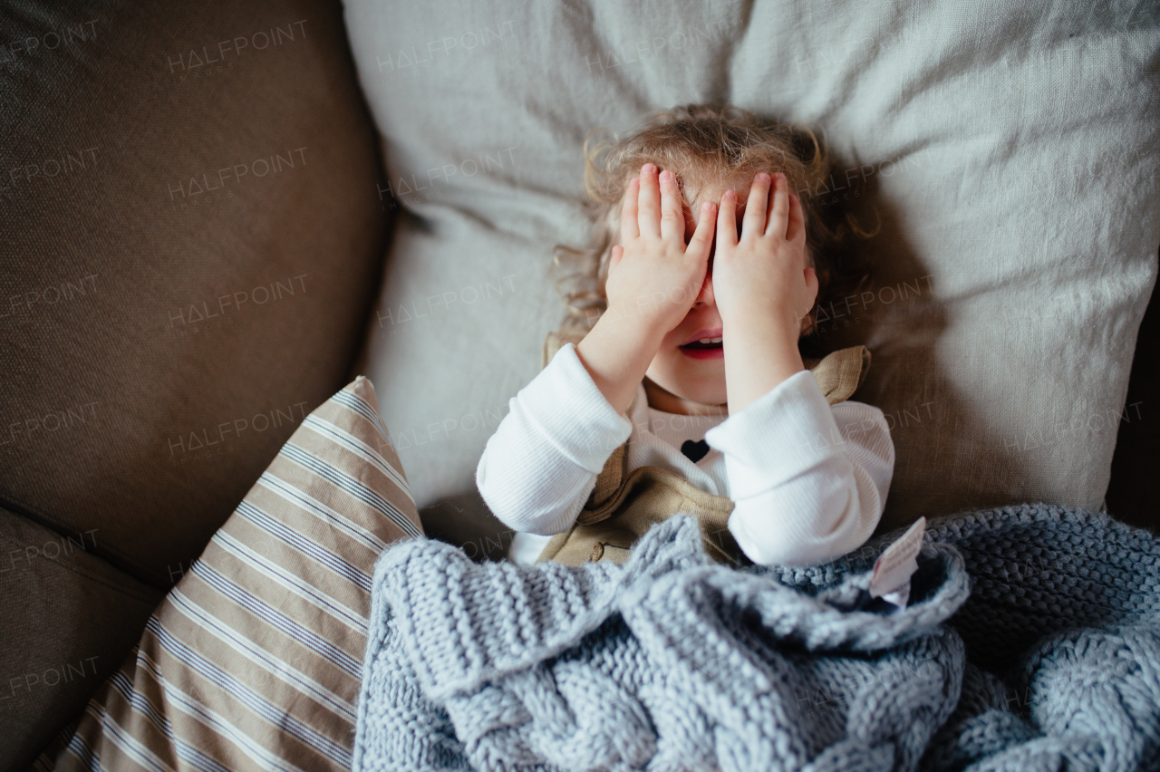 Sick girl with fever and cold lying on sofa, feeling tired, covering her face with hands