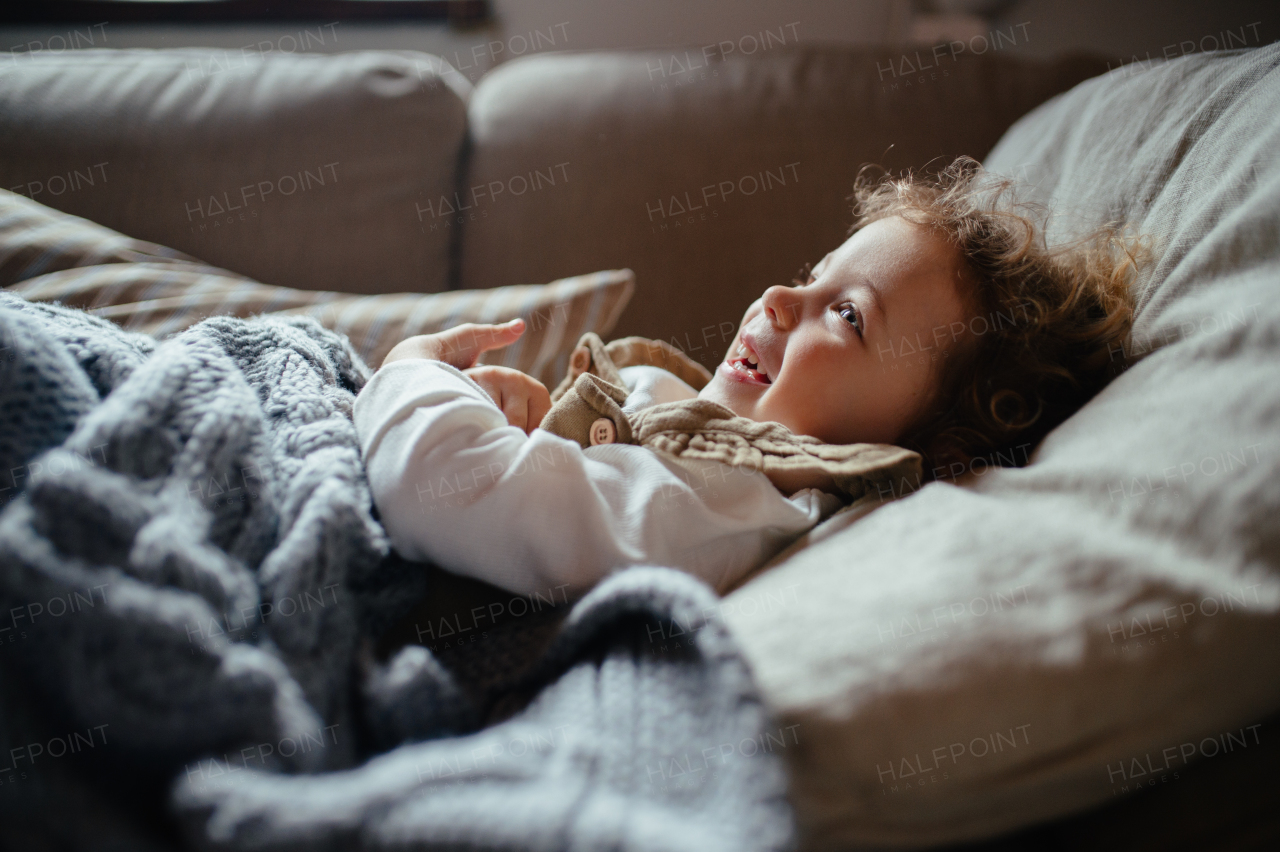 Sick girl with fever and cold lying on sofa under blanket, feeling very tired.