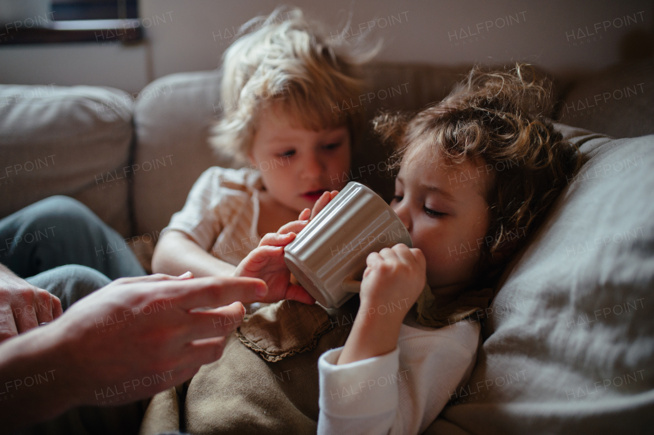 Siblings sitting on sofa, both very sick. Drinking hot herbal tea