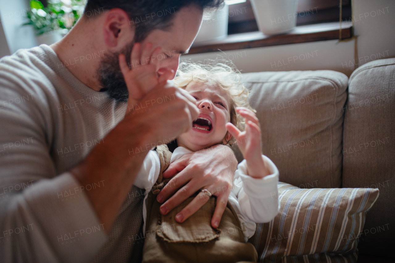 Sick girl with fever and cold at home. Father holding crying daughter