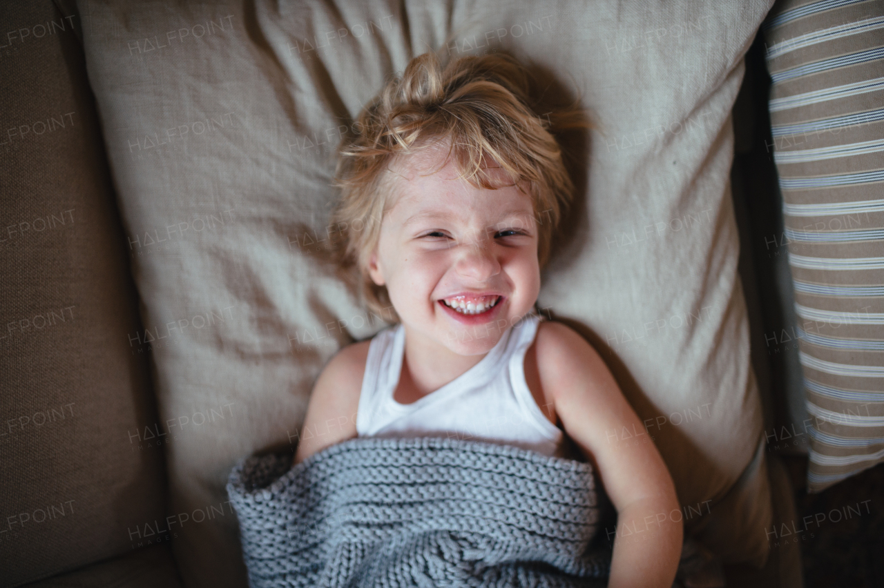 Sick boy with fever and cold lying on sofa, under blanket and smiling. Top view.