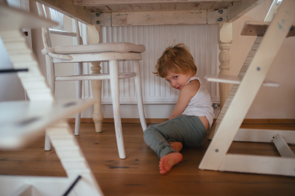 Portrait of an adorable little boy sleepy in the morning, sitting under the table in kitchen.