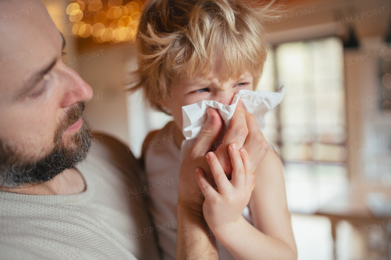 Sick boy with cold at home. Father helping little son to blow his nose