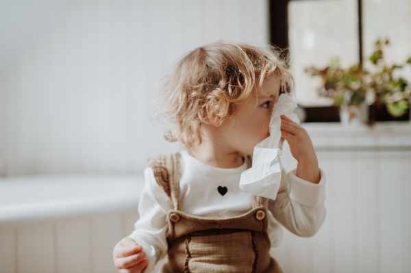 Sick girl with cold at home, blowing her nose