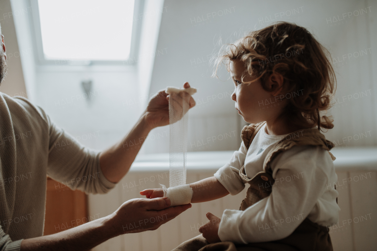 Father is bandaging his daughter's injured wrist in bathroom, concentrating while using a bandage