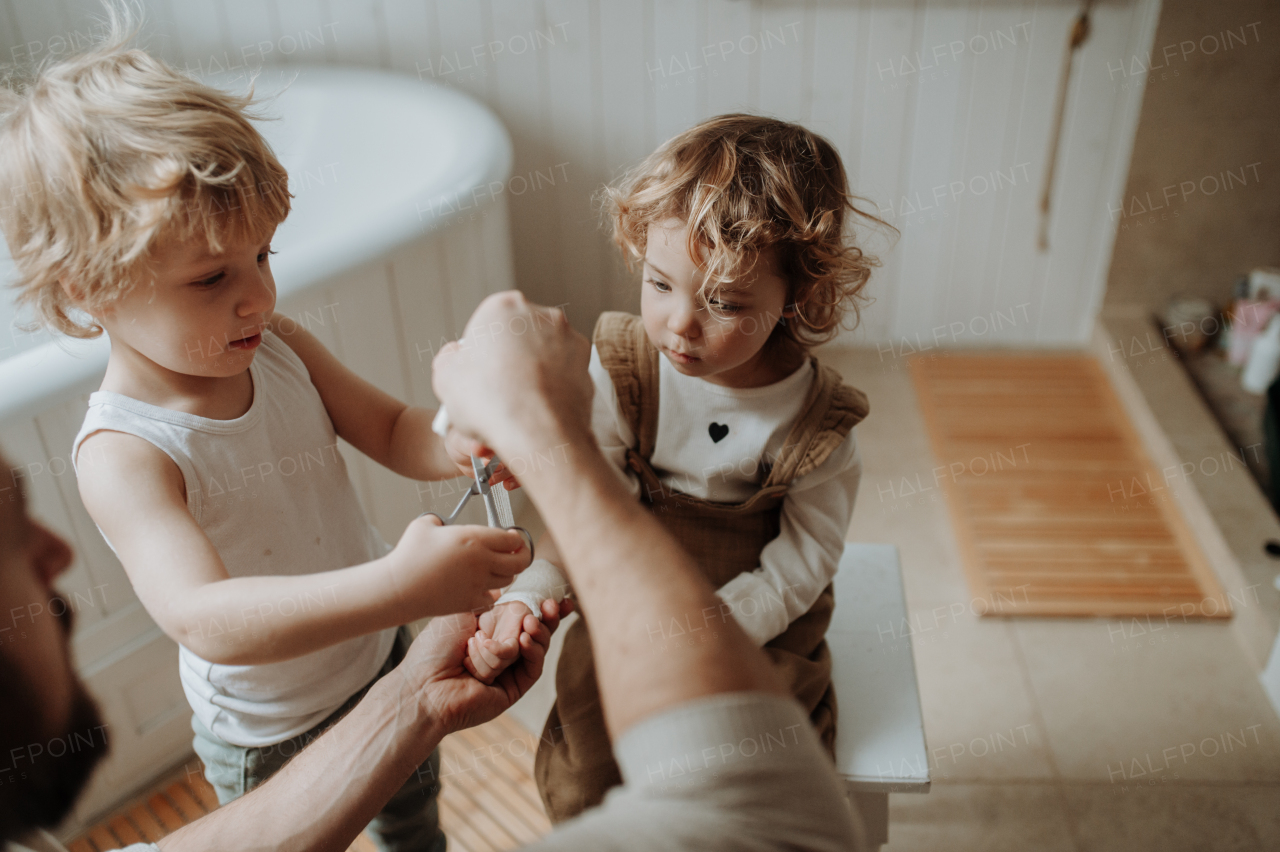 Father is bandaging his daughter's injured wrist in bathroom, concentrating while using a bandage