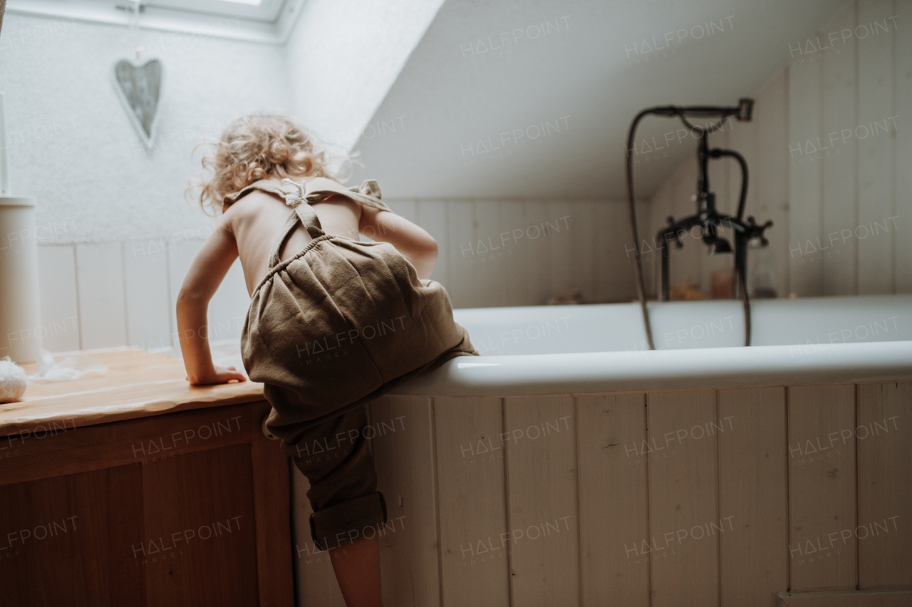 Little girl is climbing into an empty bathtub in the bathroom