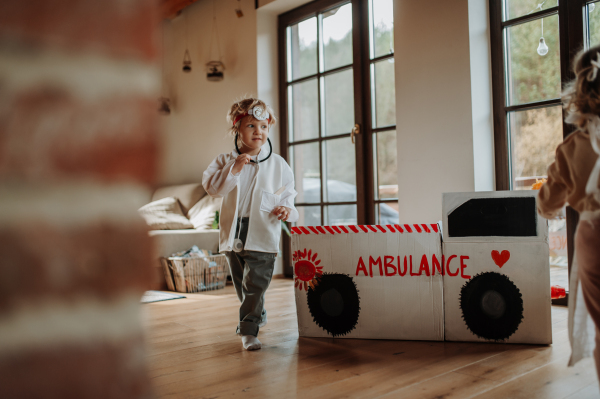 Boy in doctor uniform is playing hospital. Little ambulance paramedic sitting in cardboard ambulance