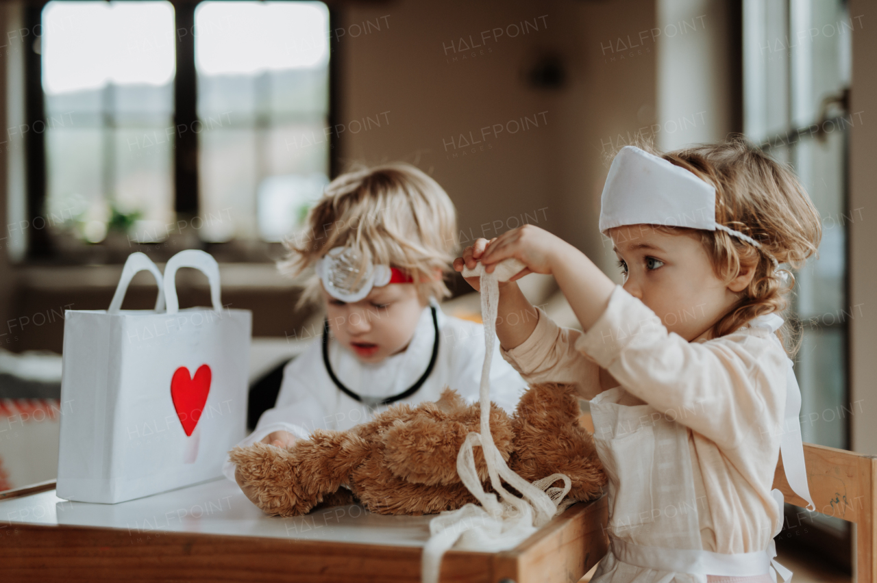 Siblings in doctor uniforms are playing hospital together, taking care of sick teddy bear.