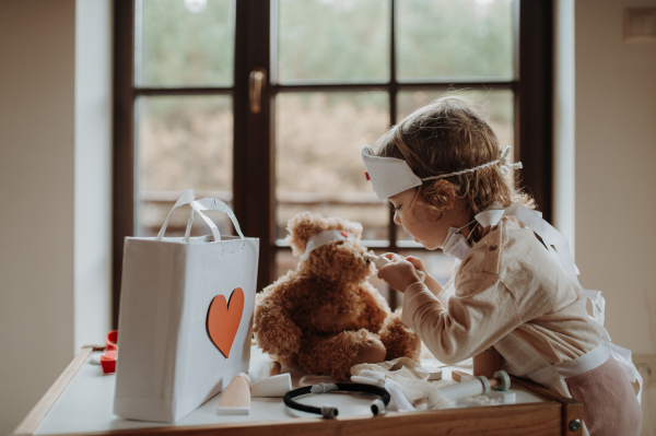 Girl in doctor uniform is playing hospital. Little girl as nurse taking care of sick teddy bear