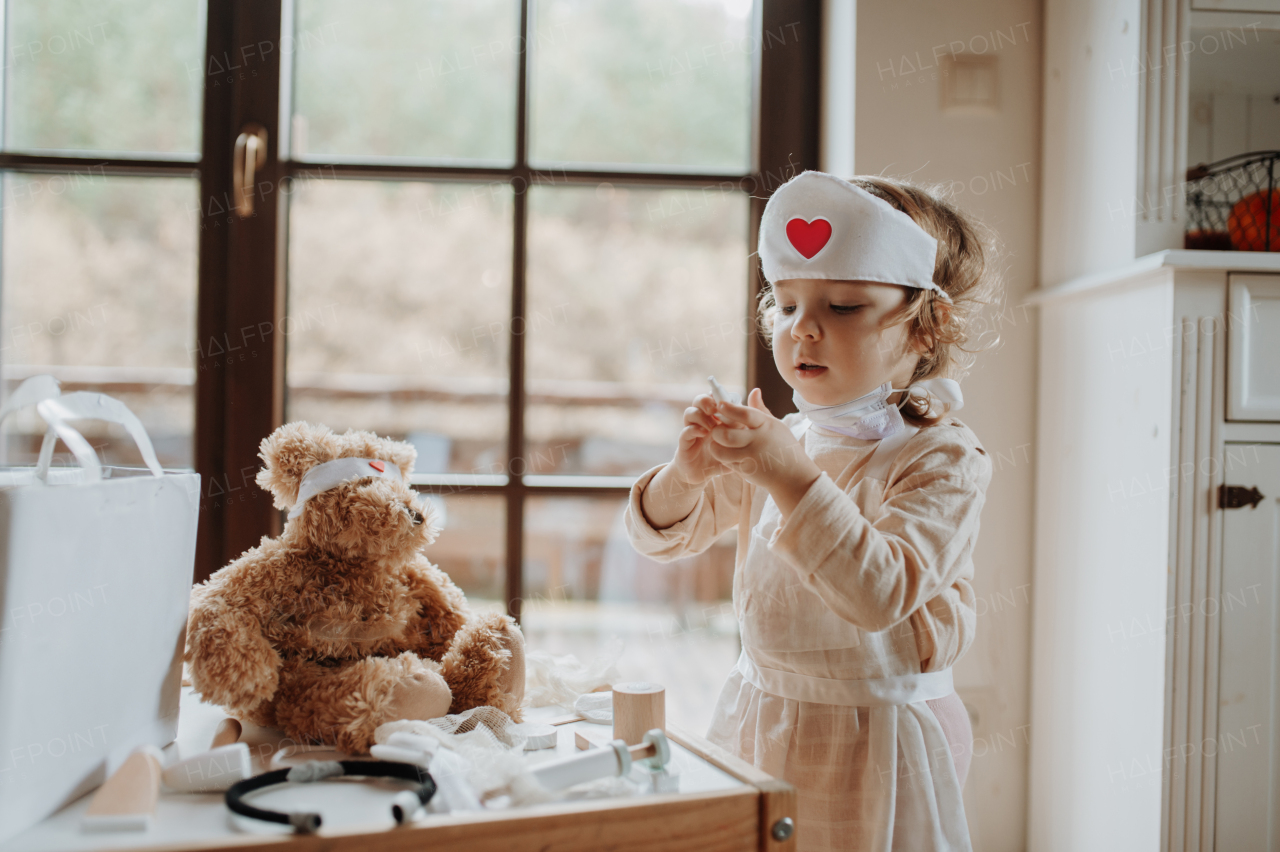 Girl in doctor uniform is playing hospital. Little girl as nurse taking care of sick teddy bear