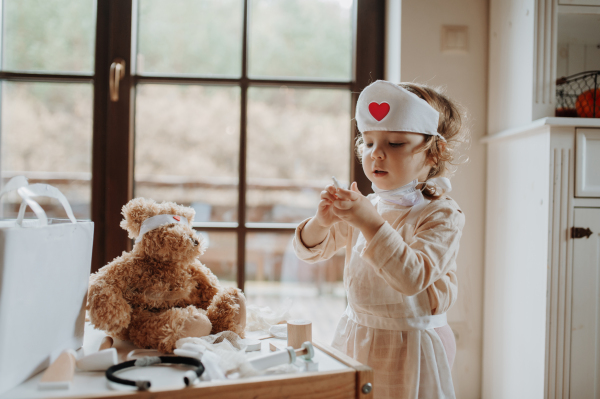 Girl in doctor uniform is playing hospital. Little girl as nurse taking care of sick teddy bear