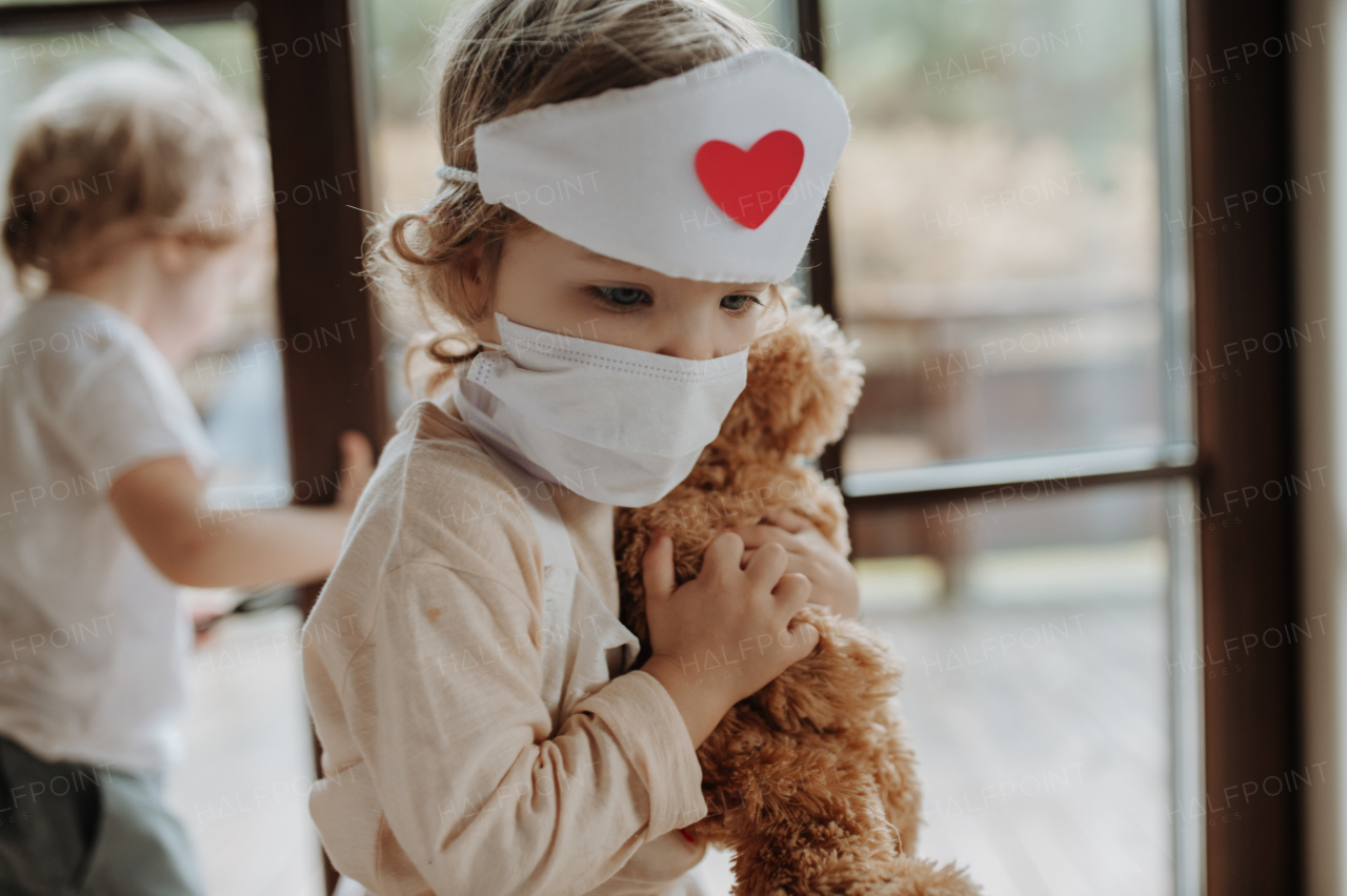 Siblings in doctor uniforms are playing hospital. Little girl as nurse taking care of sick teddy bear