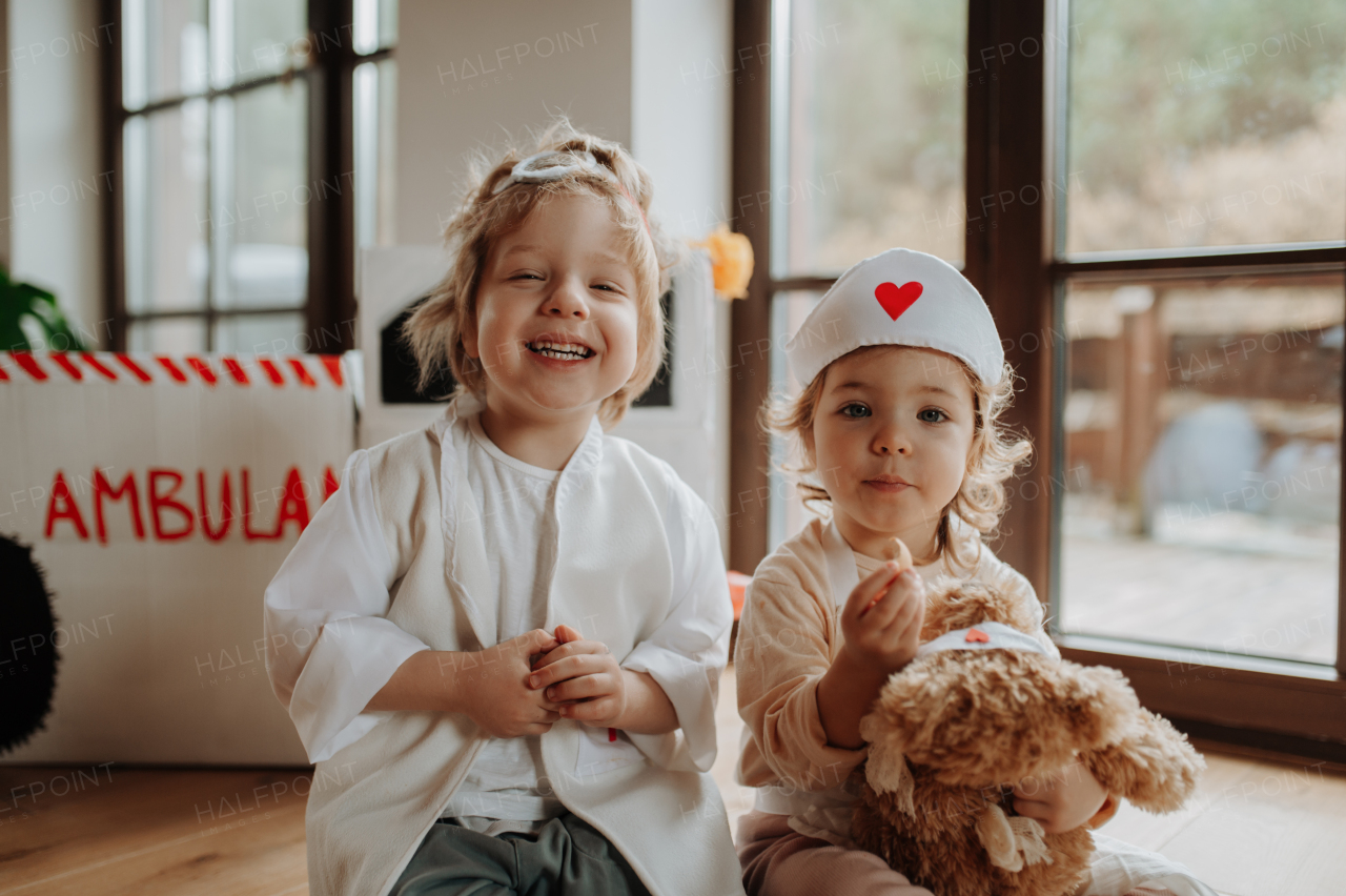 Siblings in doctor uniforms are playing hospital together, taking care of sick teddy bear.