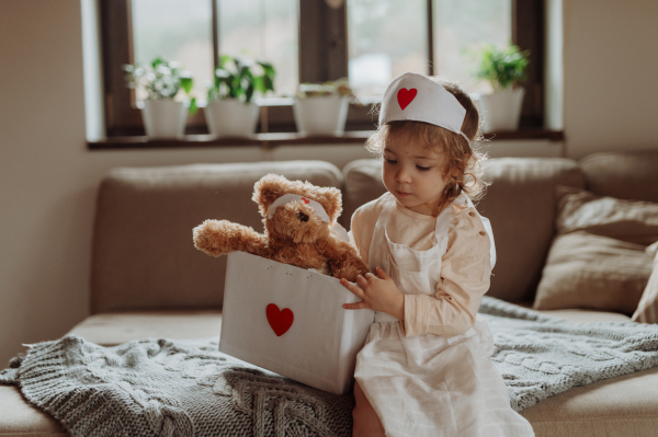 Girl in doctor uniform is playing hospital. Little girl as nurse taking care of sick teddy bear