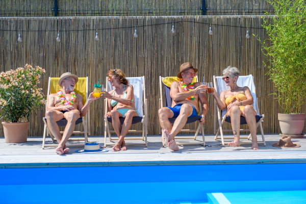 Group of cheerful seniors lying on lounge chairs by a swimming pool and sunbathing. Spending hot day outdoors in backyard.