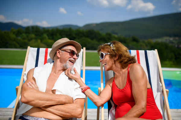 Beautiful elderly couple enjoying their vacation. Seniors having a romantic time, sitting by swimming pool in lounche chairs sunbathing.