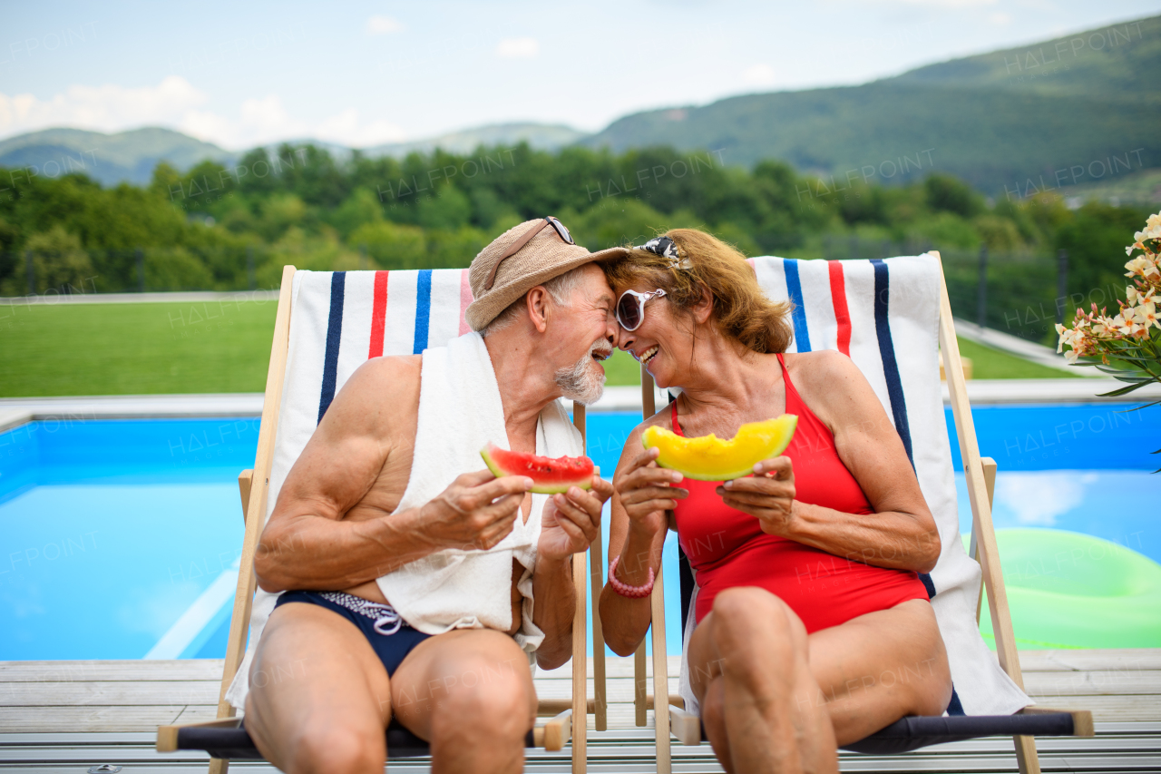 Beautiful elderly couple enjoying their vacation. Seniors having a romantic time, sitting by swimming pool in lounche chairs sunbathing.