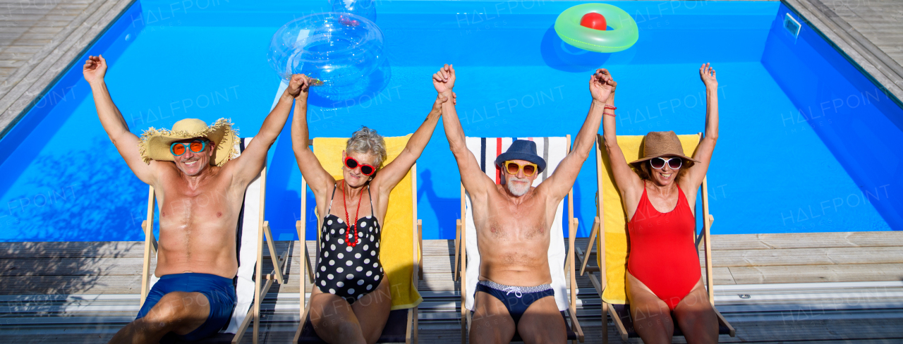 Group of cheerful seniors lying on lounge chairs by a swimming pool and sunbathing. Spending hot day outdoors in backyard. Banner with copy space.