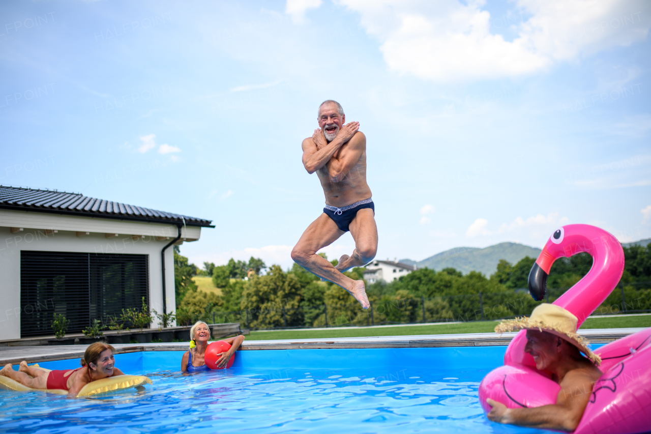 Group of cheerful seniors shaving fun in pool jumping, swiming and splashing. Elderly friends spending a hot day by swimming pool.