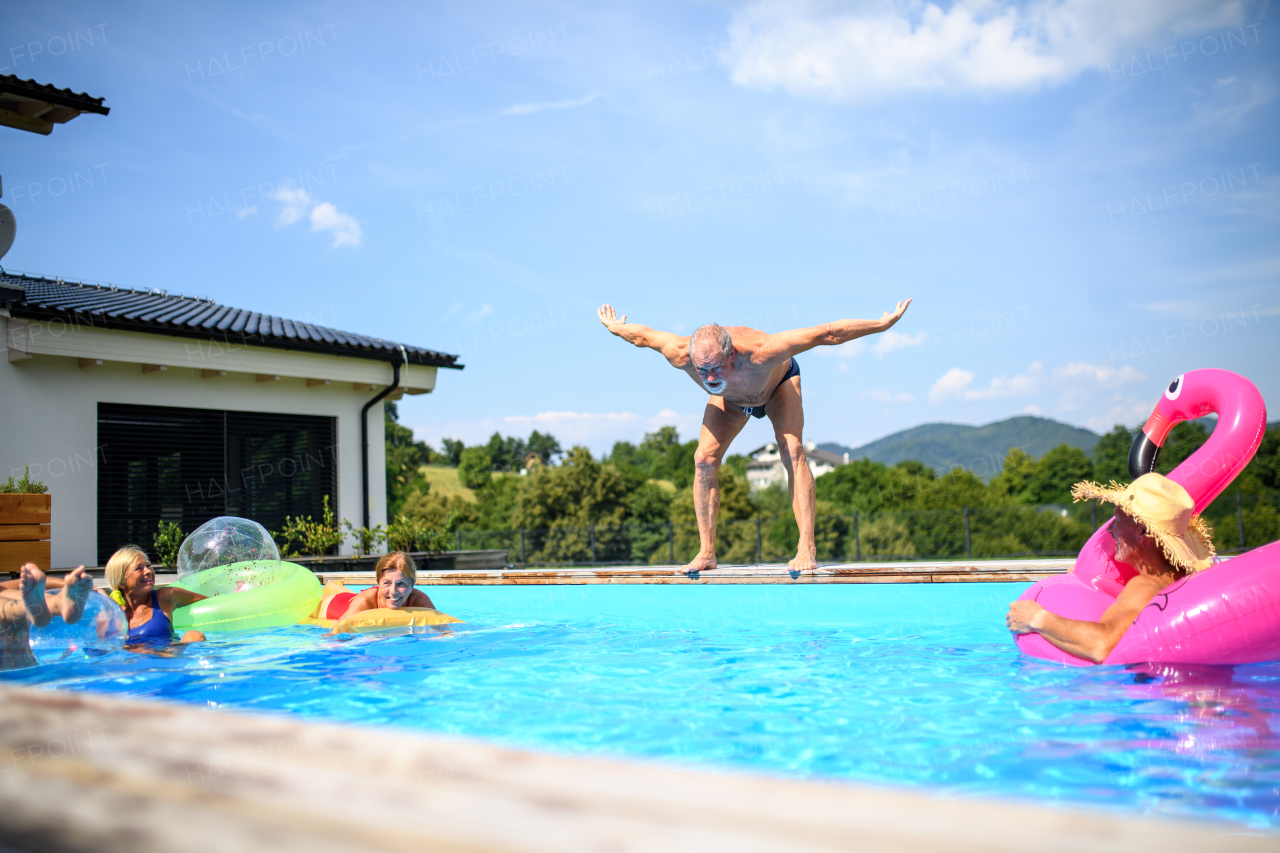 Group of cheerful seniors shaving fun in pool jumping, swiming and splashing. Elderly friends spending a hot day by swimming pool.