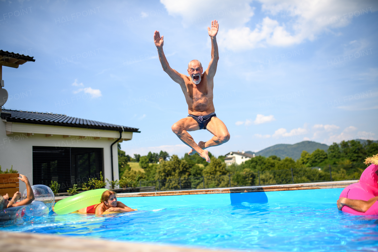 Group of cheerful seniors shaving fun in pool jumping, swiming and splashing. Elderly friends spending a hot day by swimming pool.