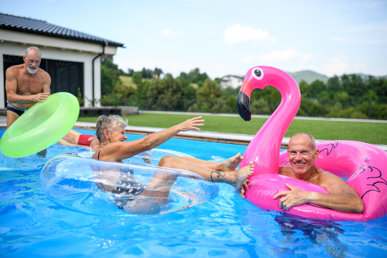 Group of cheerful seniors shaving fun in pool jumping, swiming and lounging on floats. Elderly friends spending a hot day by swimming pool.