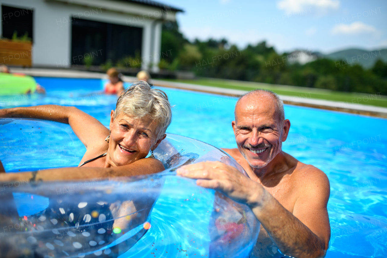 Group of cheerful seniors shaving fun in pool jumping, swiming and lounging on floats. Elderly friends spending a hot day by swimming pool.