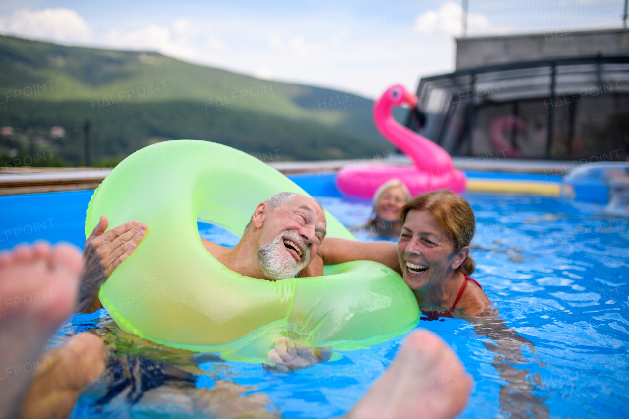 Group of cheerful seniors shaving fun in pool jumping, swiming and lounging on floats. Elderly friends spending a hot day by swimming pool.