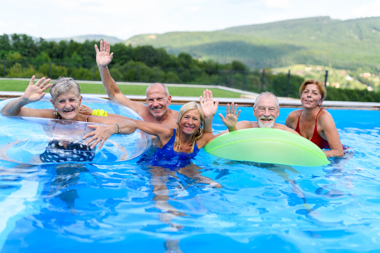 Group of cheerful seniors shaving fun in pool jumping, swiming and lounging on floats. Elderly friends spending a hot day by swimming pool.