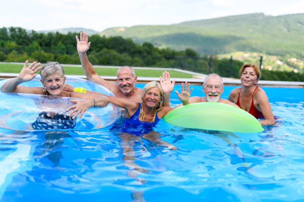 Group of cheerful seniors shaving fun in pool jumping, swiming and lounging on floats. Elderly friends spending a hot day by swimming pool.