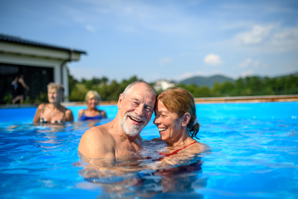 Group of cheerful seniors shaving fun in pool jumping, swiming and lounging on floats. Elderly friends spending a hot day by swimming pool.