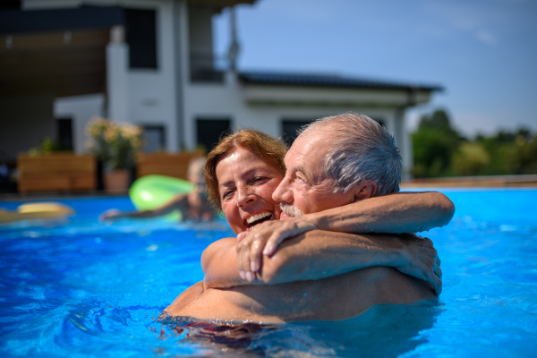 Couple of cheerful seniors shaving fun in pool with friends jumping, swiming and lounging on floats. Elderly friends spending a hot day by swimming pool.