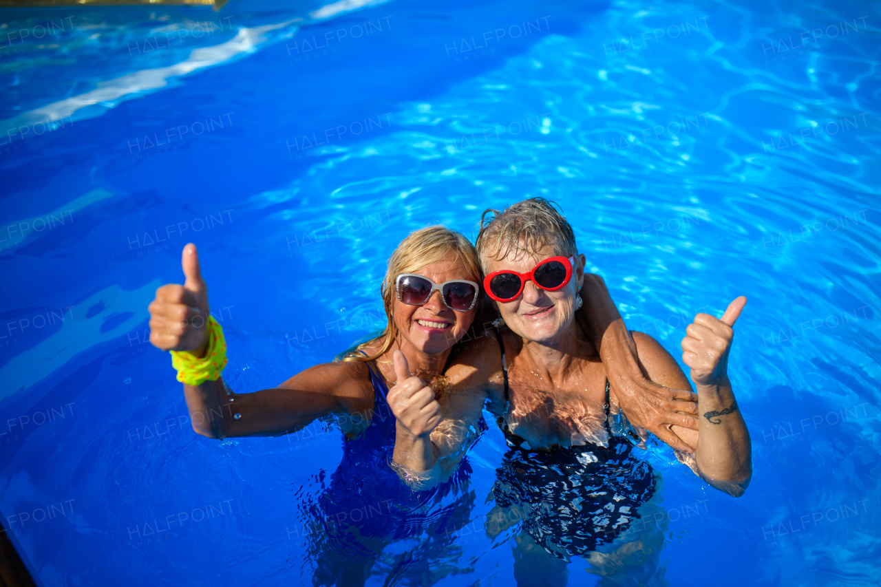 Group of cheerful seniors shaving fun in pool jumping, swiming and lounging on floats. Elderly friends spending a hot day by swimming pool.