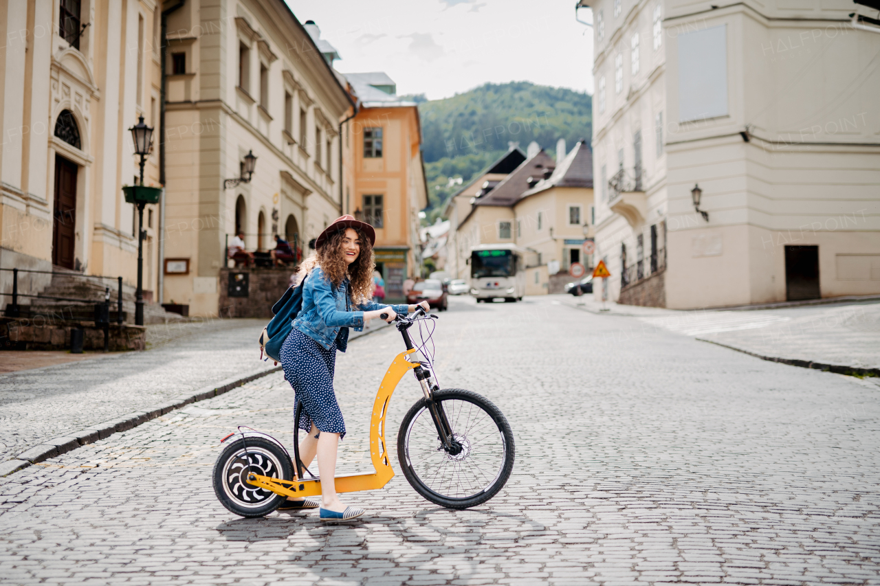 Female traveller on electric scooter in small city, sightseeing. Beautiful tourist using bike during her summer solo trip, vacation.