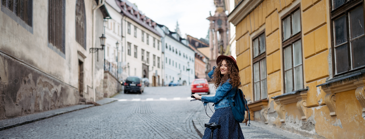 Female traveller on electric scooter in small city, sightseeing. Beautiful tourist using bike during her summer solo trip, vacation. Banner with copyspace.